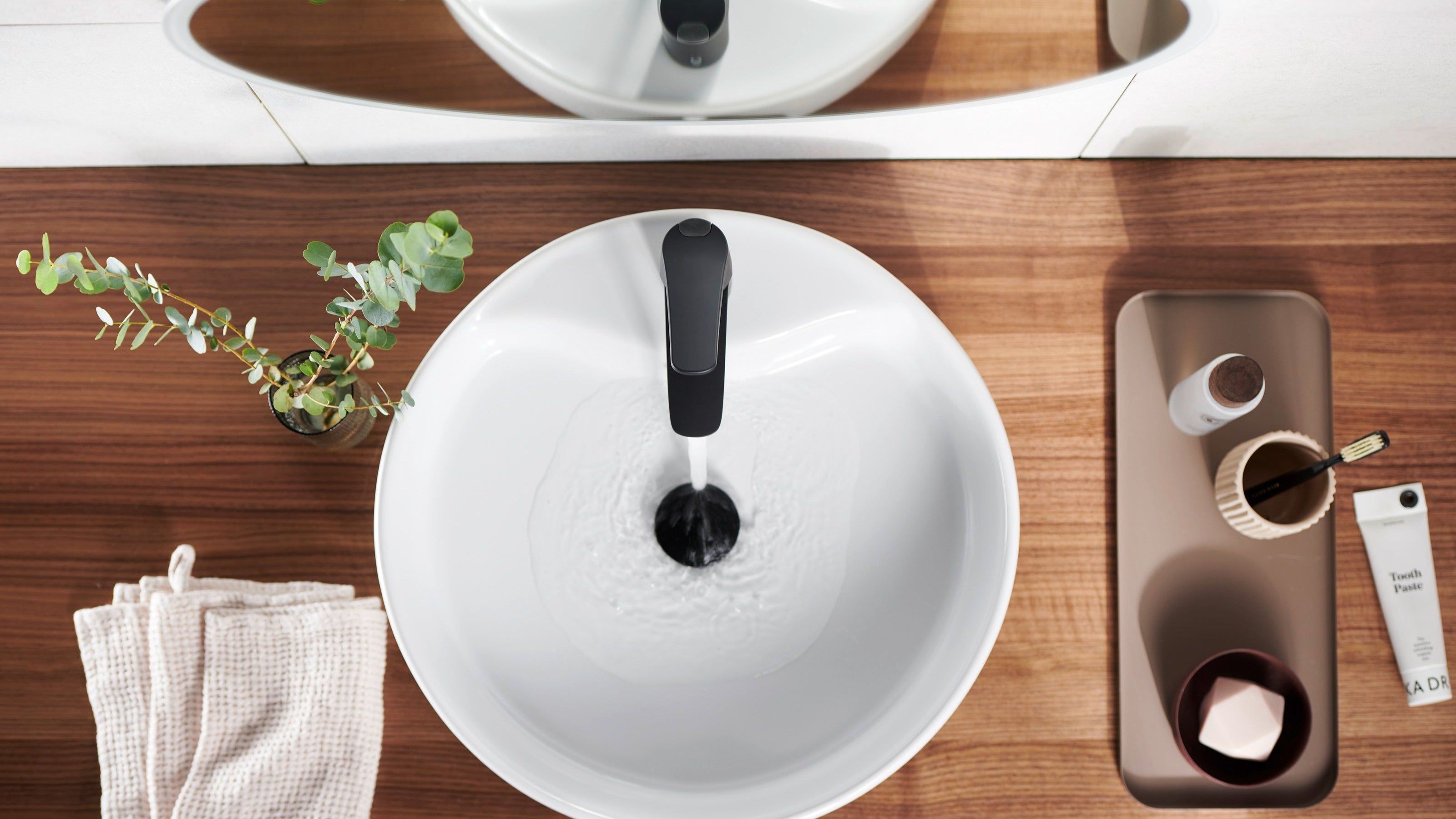 Modern bathroom setup with a white sink, black faucet, and various toiletries on a wooden counter.